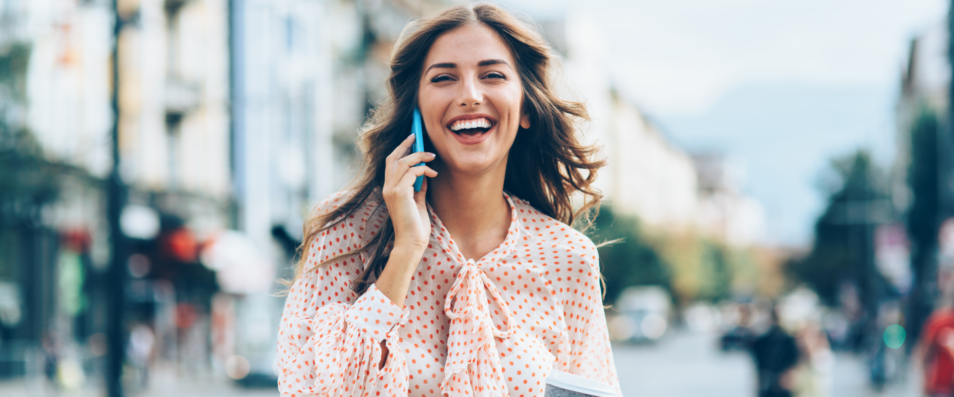Uśmiechnięta elegancka kobieta rozmawia przez telefon w centrum miasta.